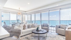 A spacious living area with a large sofa, armchairs, and a coffee table, featuring a view of the ocean through floor-to-ceiling windows. - Encantame Towers Viento 1905 (Puerto Peñasco)