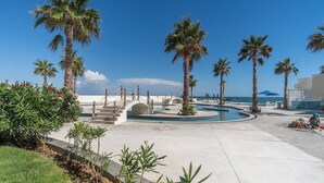 A resort pool area with palm trees, a clear blue sky, and a view of the ocean. - Perfect Family 2 Bedroom Condo E1804 Encantame (Puerto Peñasco)