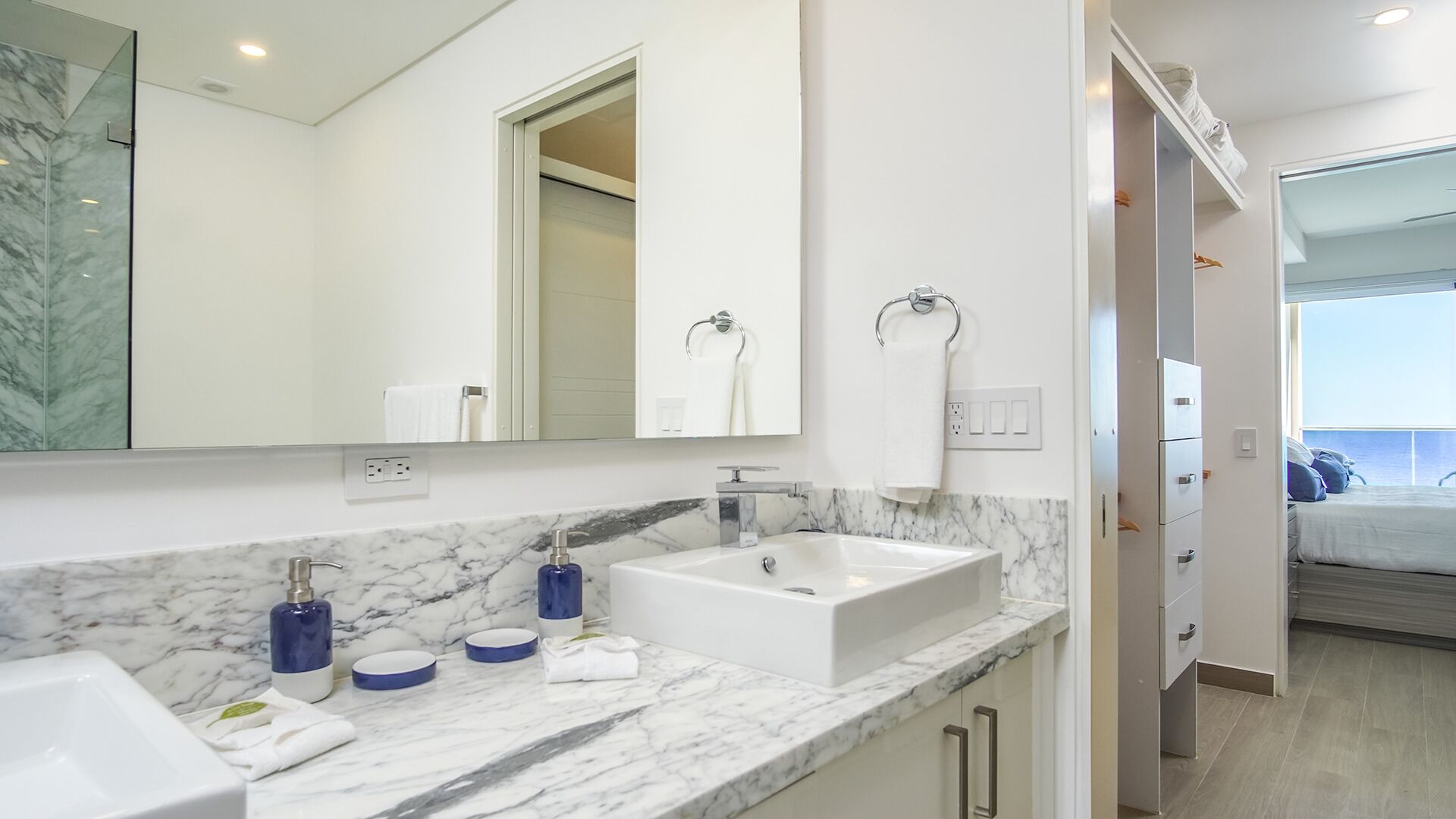 A modern bathroom with a marble countertop, a white sink, and a large mirror.
