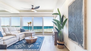 A spacious living room with a large window overlooking a beach, a ceiling fan, and a large abstract painting on the wall. - Distinctive Elegance 2 Bedroom Unit Encantame Viento 202 (Puerto Peñasco)