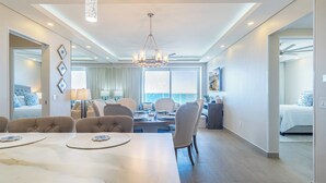 A modern hotel room with a dining area, a large chandelier, and a view of the ocean.