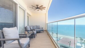 A balcony with a sofa and chairs, a ceiling fan, and a view of the ocean.