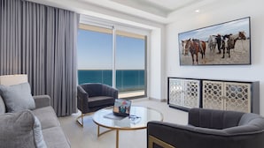 A modern living room with a large window, a ceiling fan, a laptop on a glass table, and a painting of horses on the wall. - Spectacular 2 Bedroom 2bathroom Beach Front Condominium at Encantame C1002 (Puerto Peñasco)