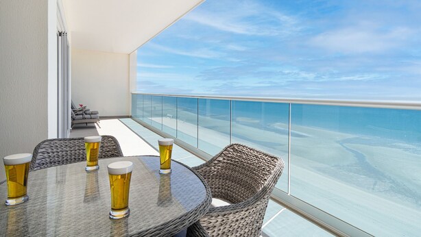 A balcony with a glass table and wicker chairs, overlooking a beach. - Spectacular 2 Bedroom 2bathroom Beach Front Condominium at Encantame C1002 (Puerto Peñasco)
