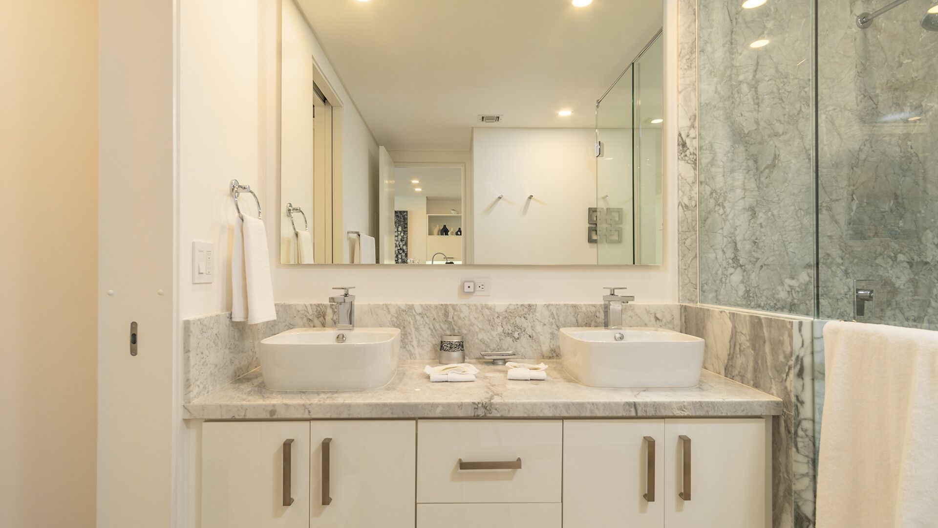 Une salle de bain moderne avec deux lavabos, un grand miroir et une douche à l’italienne.