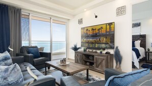 A modern living room with a large window overlooking the sea, a coffee table, sofas, and a painting on the wall. - Encantame Towers Viento 1103 (Puerto Peñasco)
