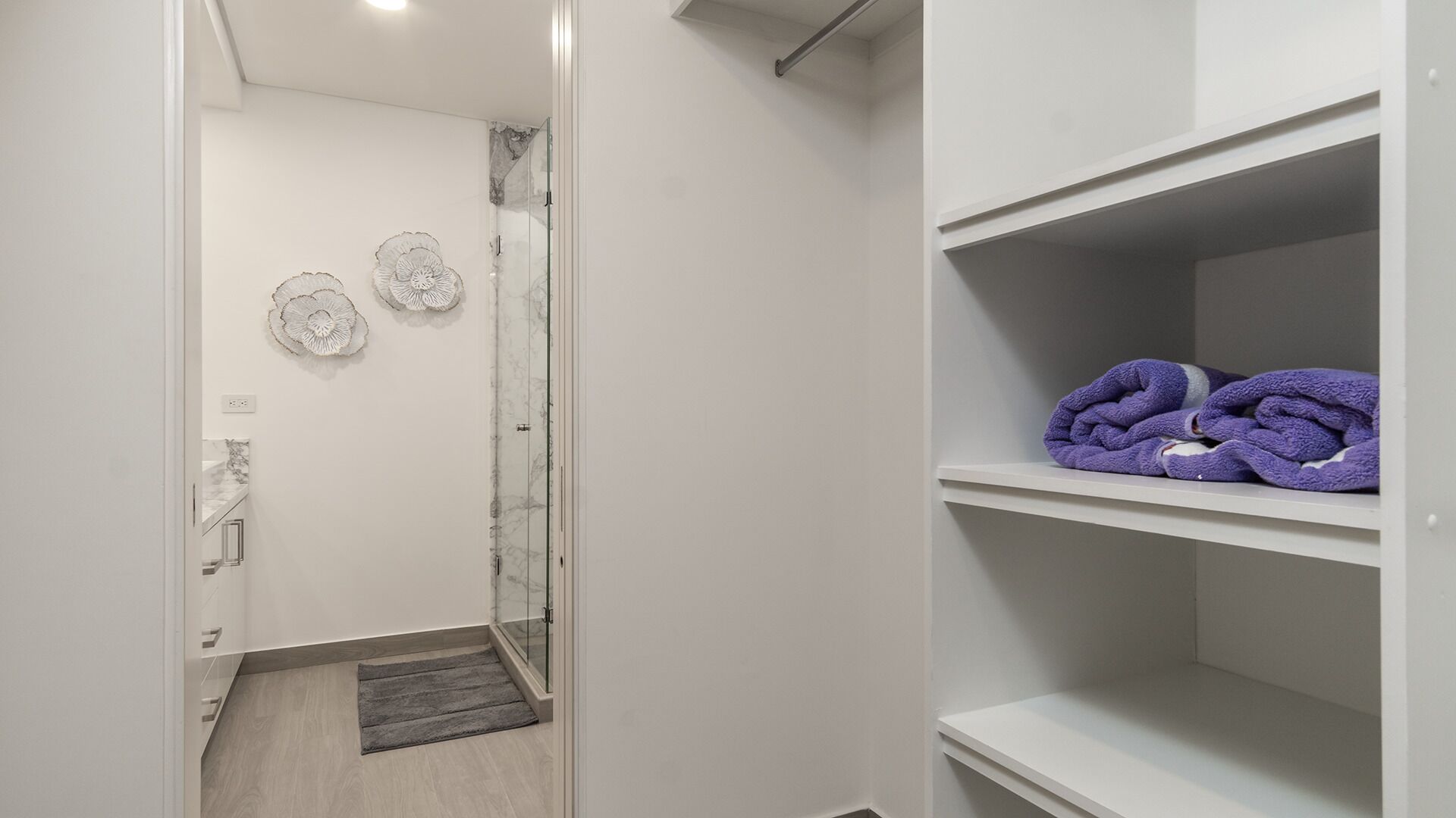 A bathroom with a glass shower door, a towel rack with towels, and a marble wall.