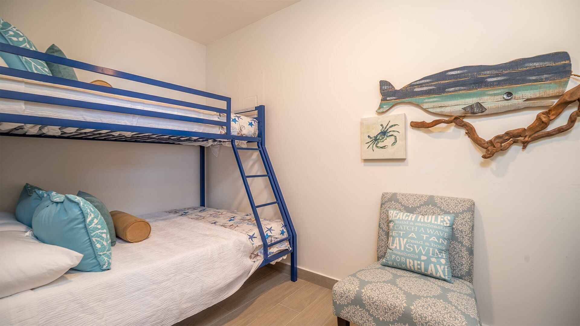 A bunk bed with a ladder, a chair with a cushion, and wall decorations including a fish and a crab.
