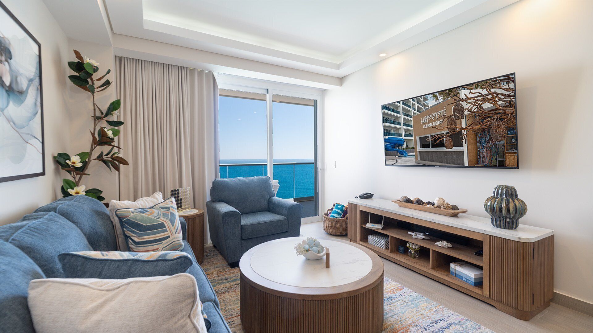 Una sala de estar moderna con sofá, sillón, mesa de centro y televisor en la pared.