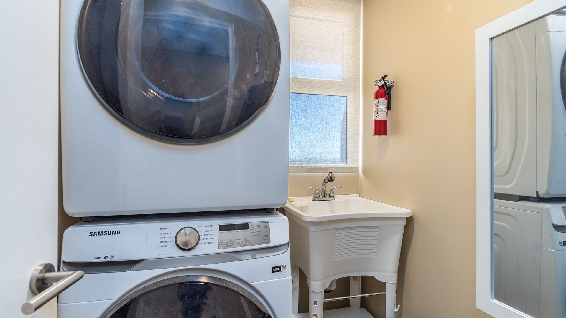A laundry room with a front-loading washer and dryer, a sink, and a fire extinguisher on the wall.
