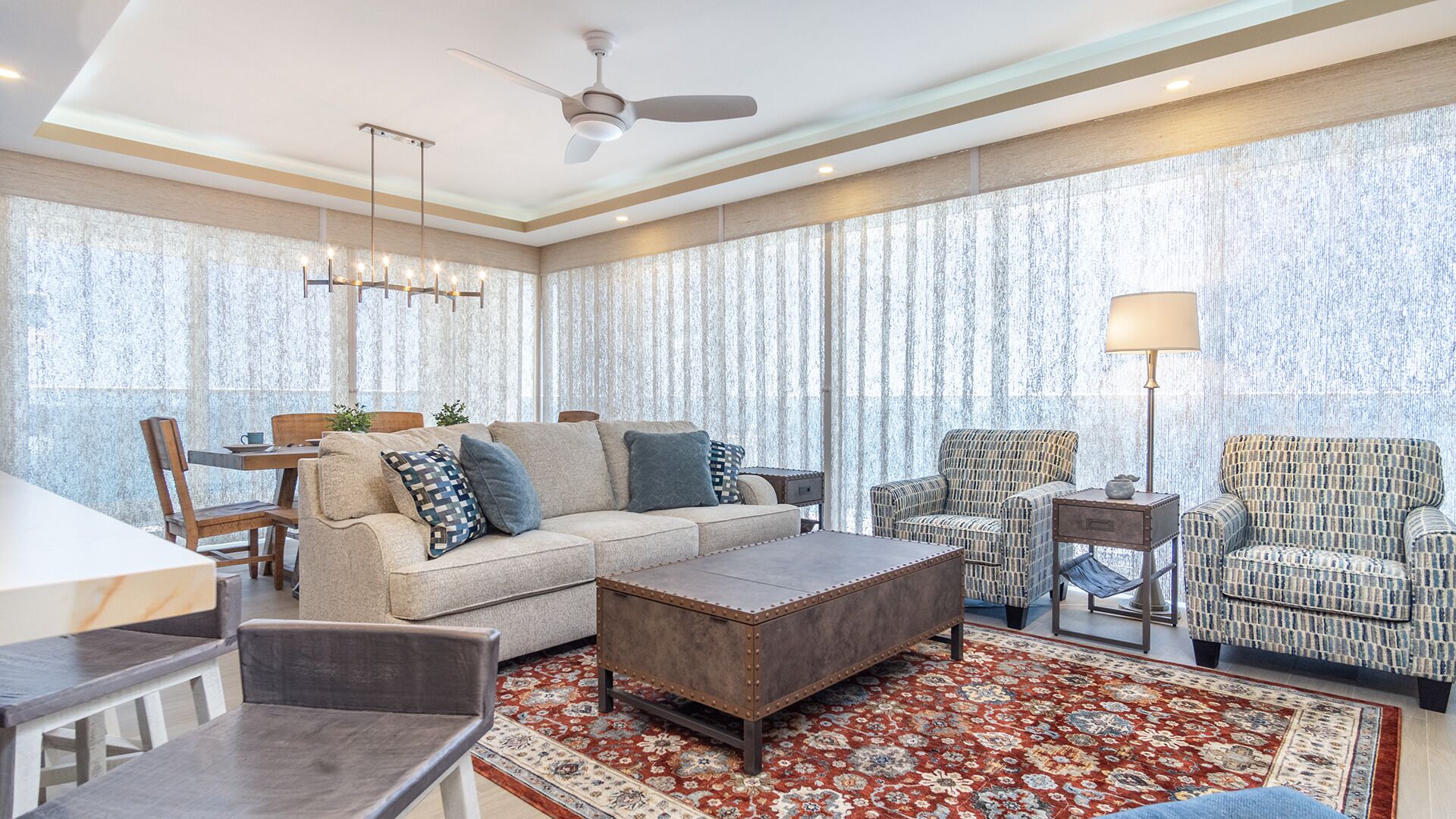 Ein geräumiges Wohnzimmer mit Sofa, Ohrensessel, Hocker und einem Essbereich mit Tisch und Stühlen.