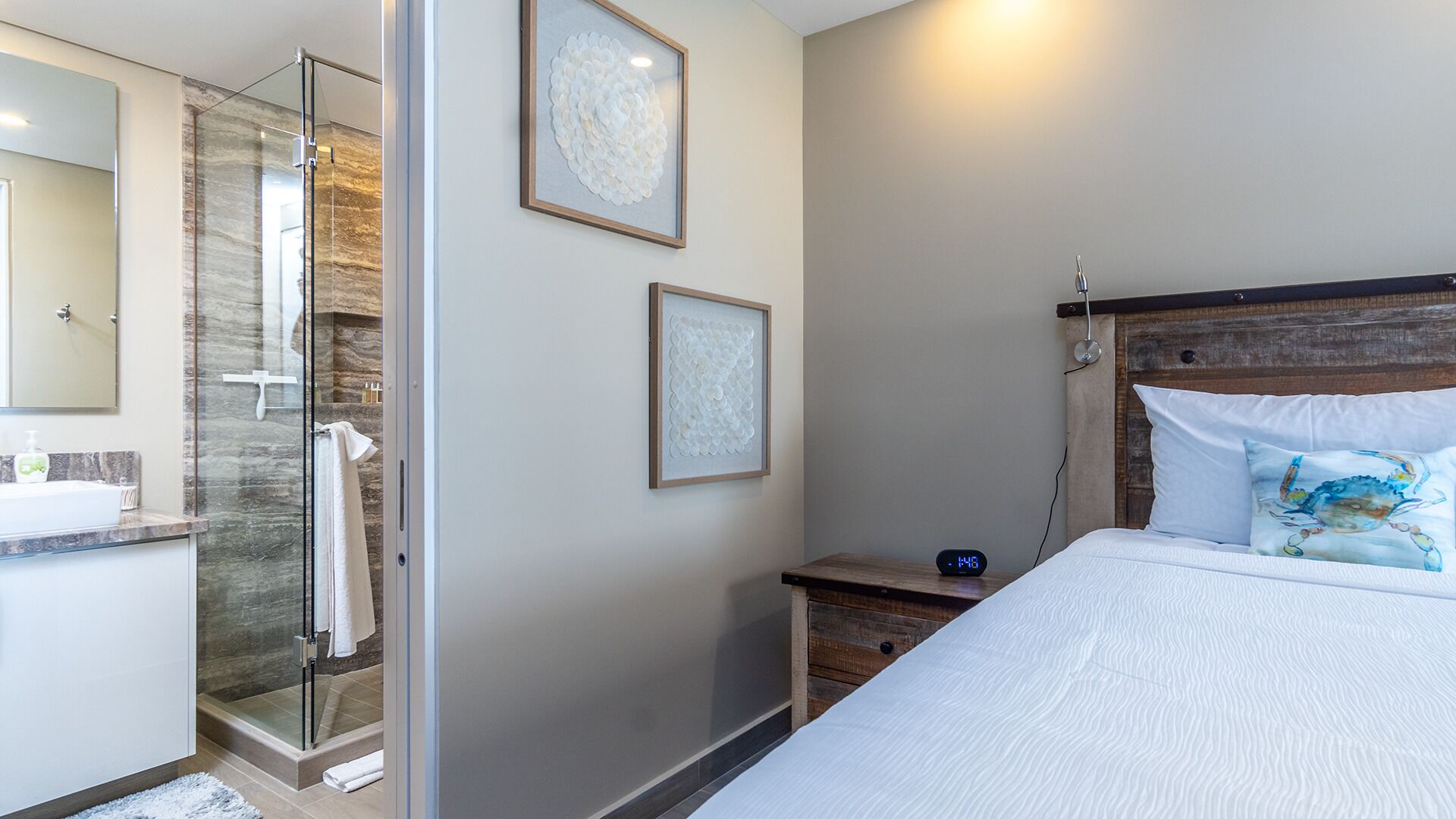 A modern bedroom with a bed, a nightstand, a digital clock, and a shower area.