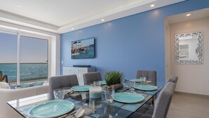 A dining area with a glass table, blue plates, and grey chairs. There is a large window with a view of the ocean. - Splash in The New Lazy River and Sleep In Luxury Encantame C-1104 (Puerto Peñasco)