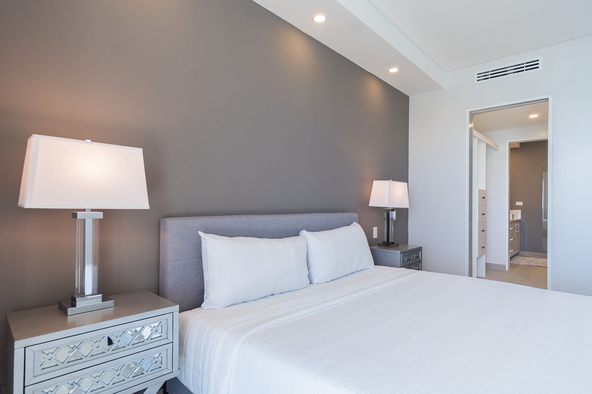 Una habitación de hotel moderna con una cama grande, dos mesitas de noche con lámparas y una decoración en tonos neutros.