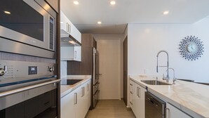 A modern kitchen with stainless steel appliances, a marble countertop, and a unique wall clock. - Splash in The New Lazy River and Sleep In Luxury Encantame C-1104 (Puerto Peñasco)