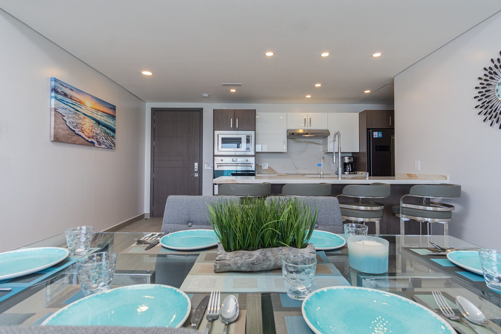 A modern dining area with a glass table, teal plates, and a central plant.