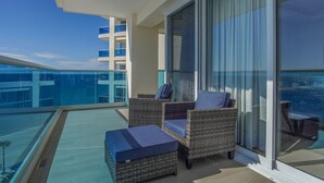 A balcony with wicker furniture and a glass railing overlooking a pool and a high-rise building. - Beautiful 2 Bedroom Condominium Fully Equipped at the New Encantame Towers Verano 805 (Puerto Peñasco)