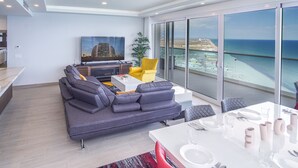 Ein modernes Wohnzimmer mit einem grauen Sofa, einem gelben Sessel und einem Essbereich mit einem weißen Tisch, gedeckt für zwei Personen.