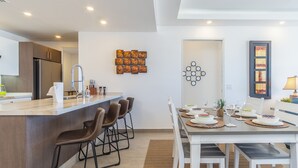 Une cuisine moderne dotée d’un îlot central, de tabourets de bar et d’une table à manger pouvant accueillir six personnes.