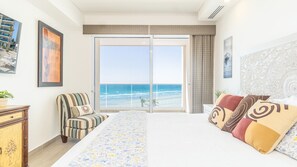 A hotel room with a large bed, a chair, a desk, and a view of the ocean. - A Sanctuary Of Tranquillity Encantame Viento 404 (Puerto Peñasco)