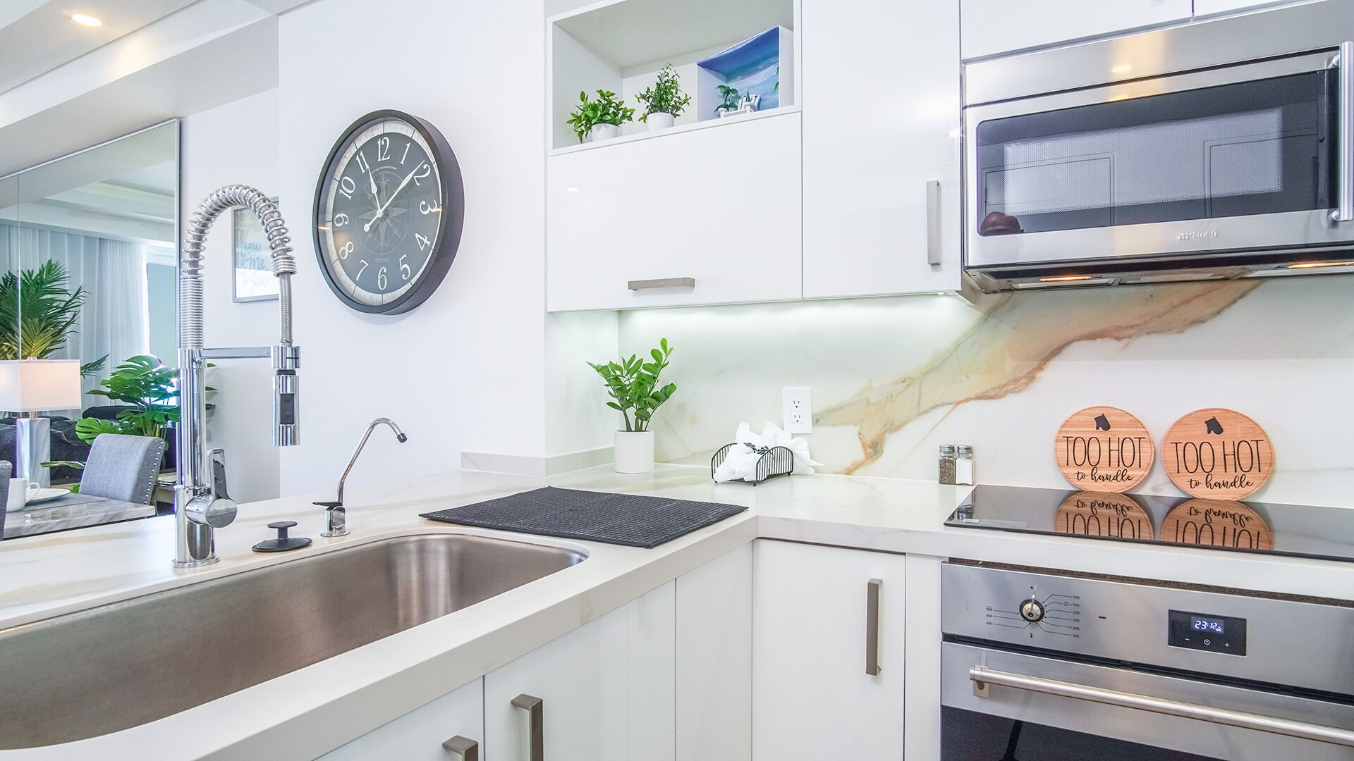 A modern kitchen with a stainless steel sink, a wall-mounted clock, a microwave, and a digital oven display.