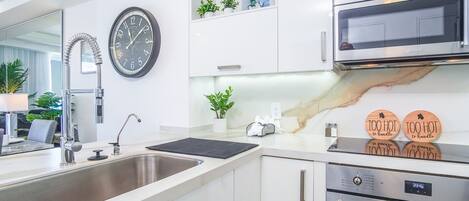 A modern kitchen with a stainless steel sink, a wall-mounted clock, a microwave, and a digital oven display.