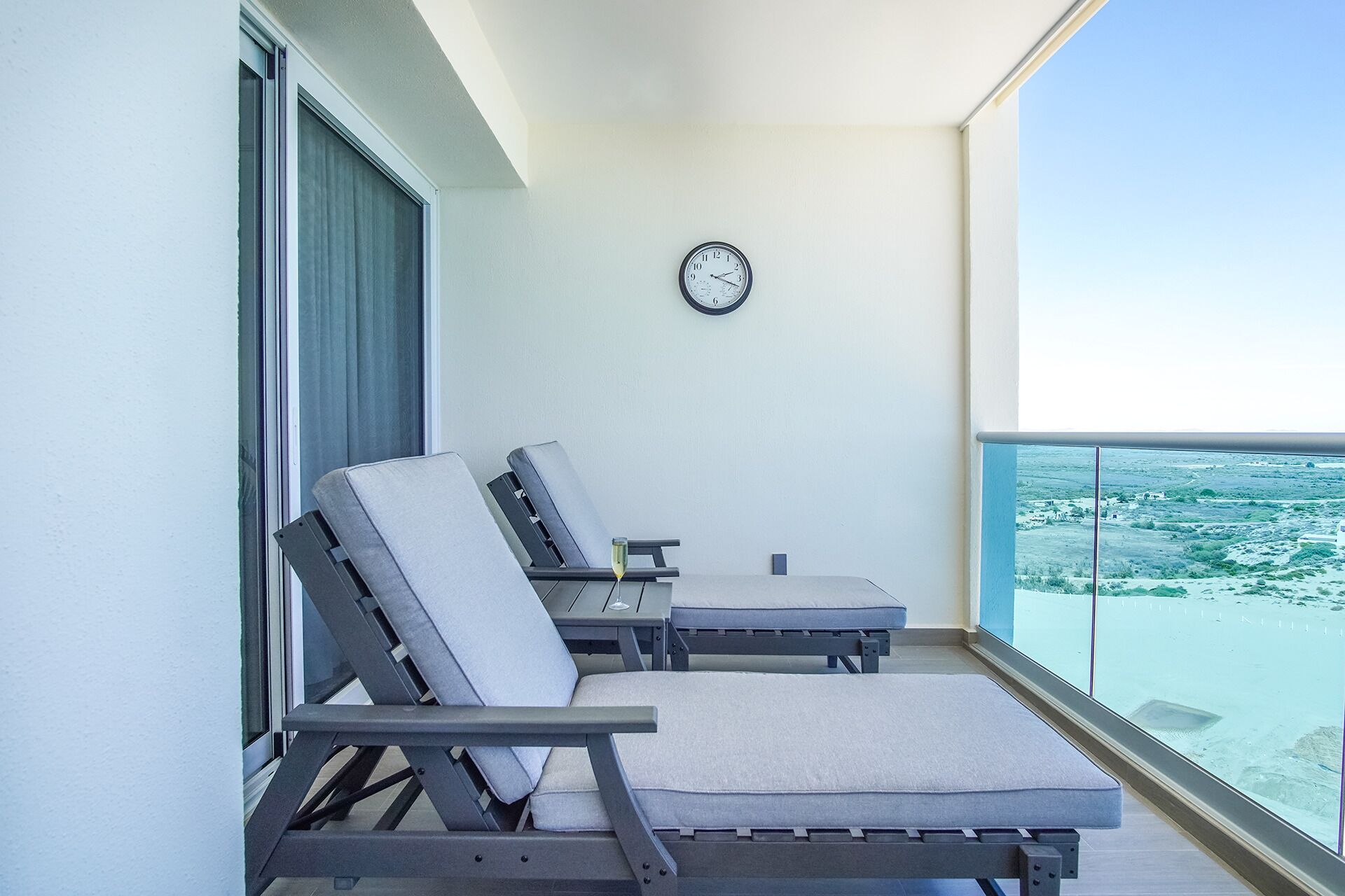 A balcony with two lounge chairs, a table, and a clock on the wall.