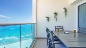 A balcony with a view of the beach and ocean. There is a table with chairs and two glasses of beer.