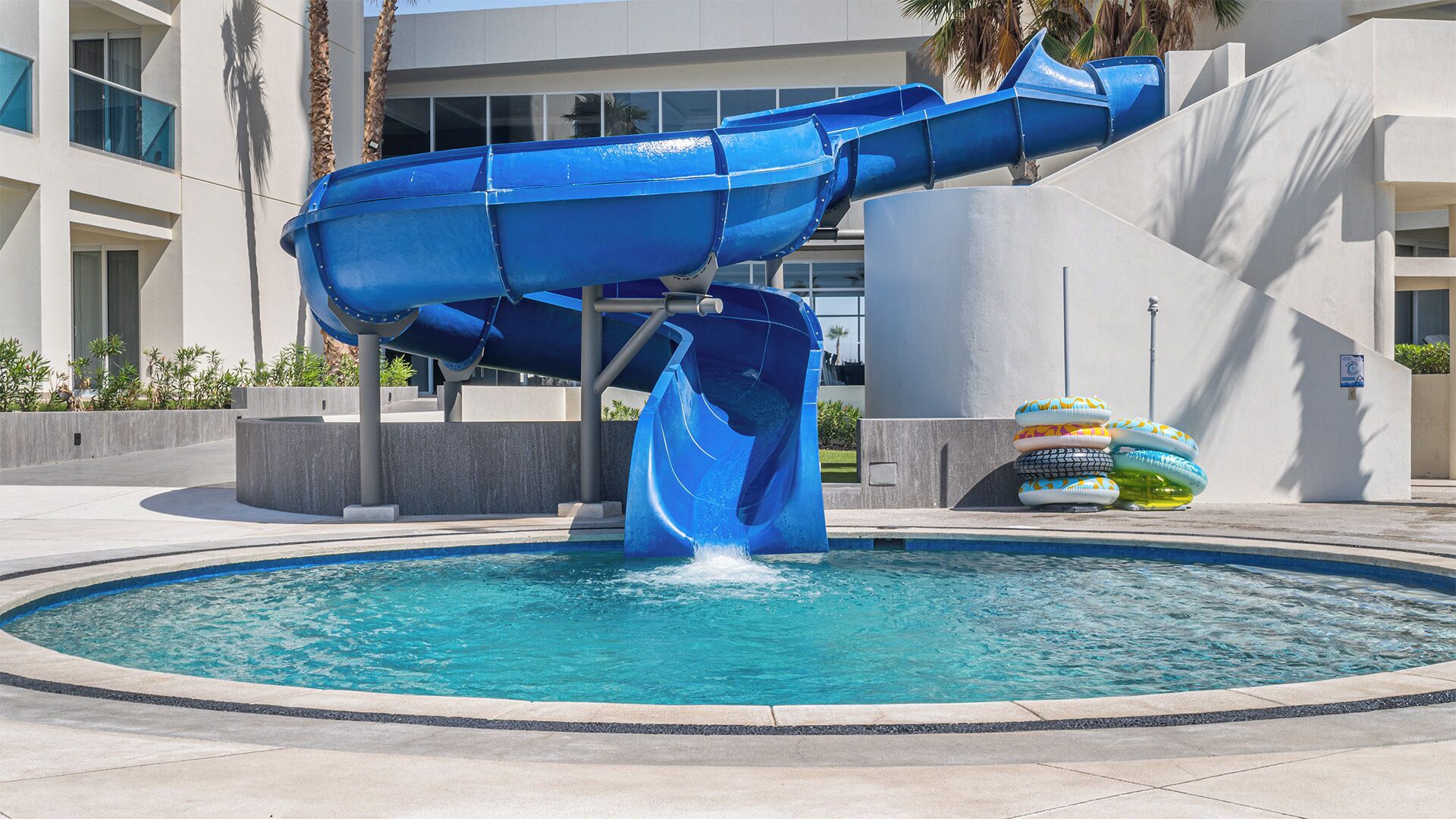 Un tobogán azul sobre una piscina con anillos inflables.