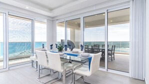 A modern dining area with a glass table and white chairs, overlooking a scenic ocean view. - Encantame Towers Viento 801 (Puerto Peñasco)