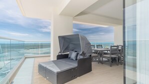 A balcony with a wicker sofa and table, overlooking a beach and ocean. - Encantame Towers Viento 801 (Puerto Peñasco)