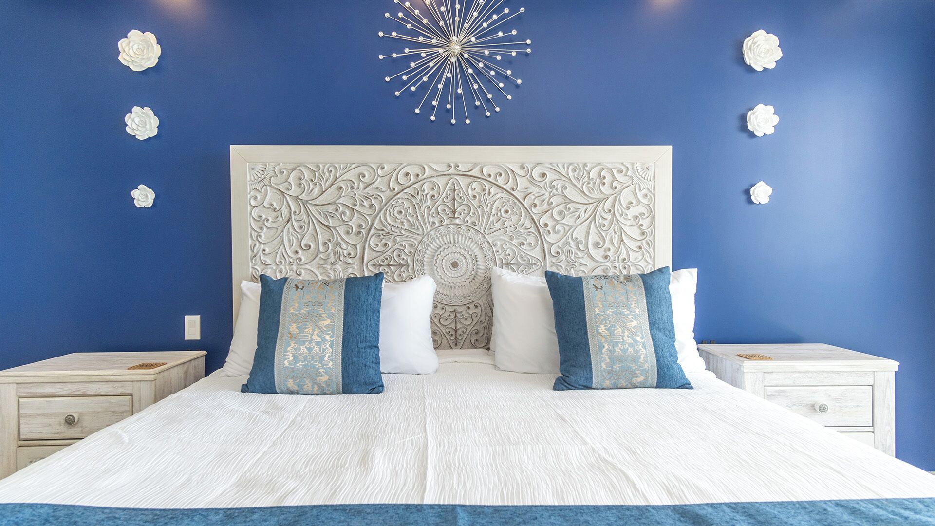 Un dormitorio con una cama grande, ropa de cama blanca, un cabecero decorativo y una pared azul de acento.