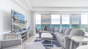 A modern living room with a large TV, a grey sofa, and a view of the sea. - Encantame Towers Viento 801 (Puerto Peñasco)
