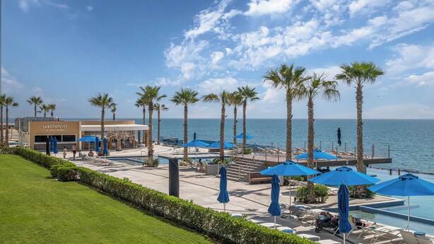 A resort pool area with palm trees, lounge chairs, and umbrellas. - Encantame Towers Viento 801 (Puerto Peñasco)