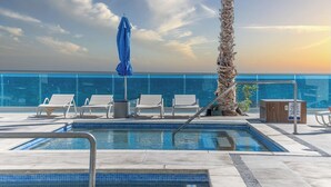 Une piscine sur le toit, avec quatre chaises longues blanches, un parasol bleu et un palmier.