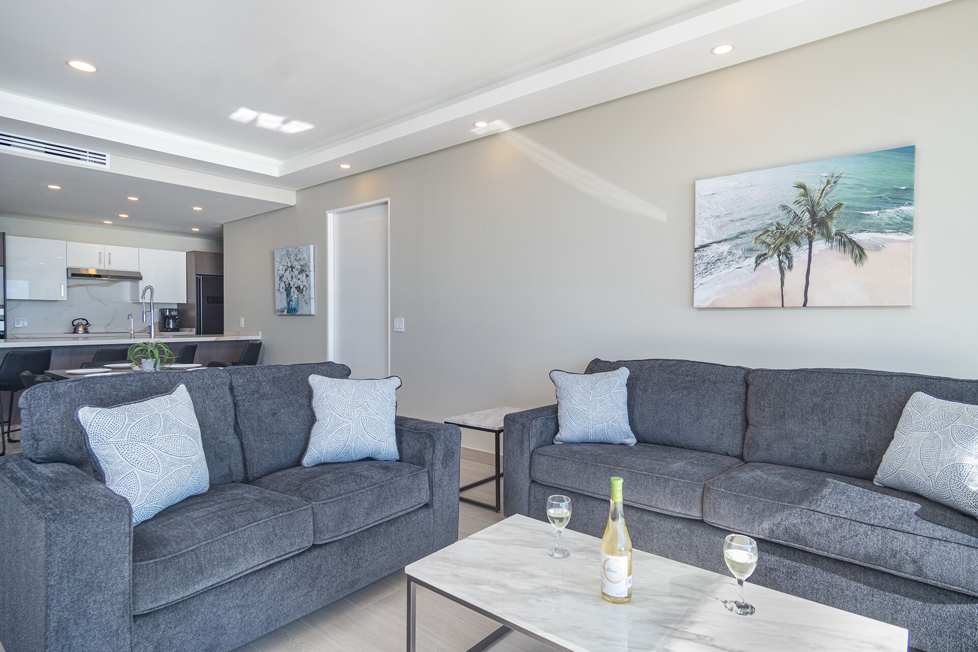 A modern living room with grey sofas, a marble coffee table, and a painting of a beach scene.
