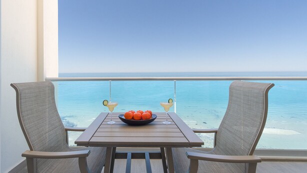 A balcony with a table and two chairs, overlooking a clear blue sea. - Splash in The New Lazy River and Sleep In Luxury Encantame Towers C 1203 (Puerto Peñasco)