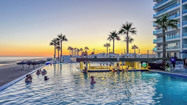 A pool area with lounge chairs and palm trees, overlooking a beach at sunset. - Looking for the Perfect Scape From the City? Peaceful 2 Bedroom Condo Verano 804 (Puerto Peñasco)