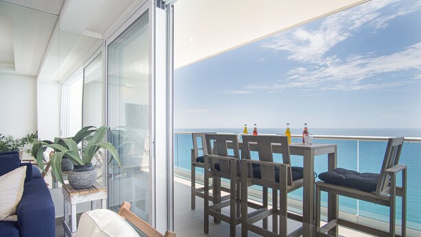 A balcony with a wooden table and chairs, overlooking the sea. - Stunning 2BR Condo at Encantame Towers Velero 2302 in Playa Encanto (Puerto Peñasco)