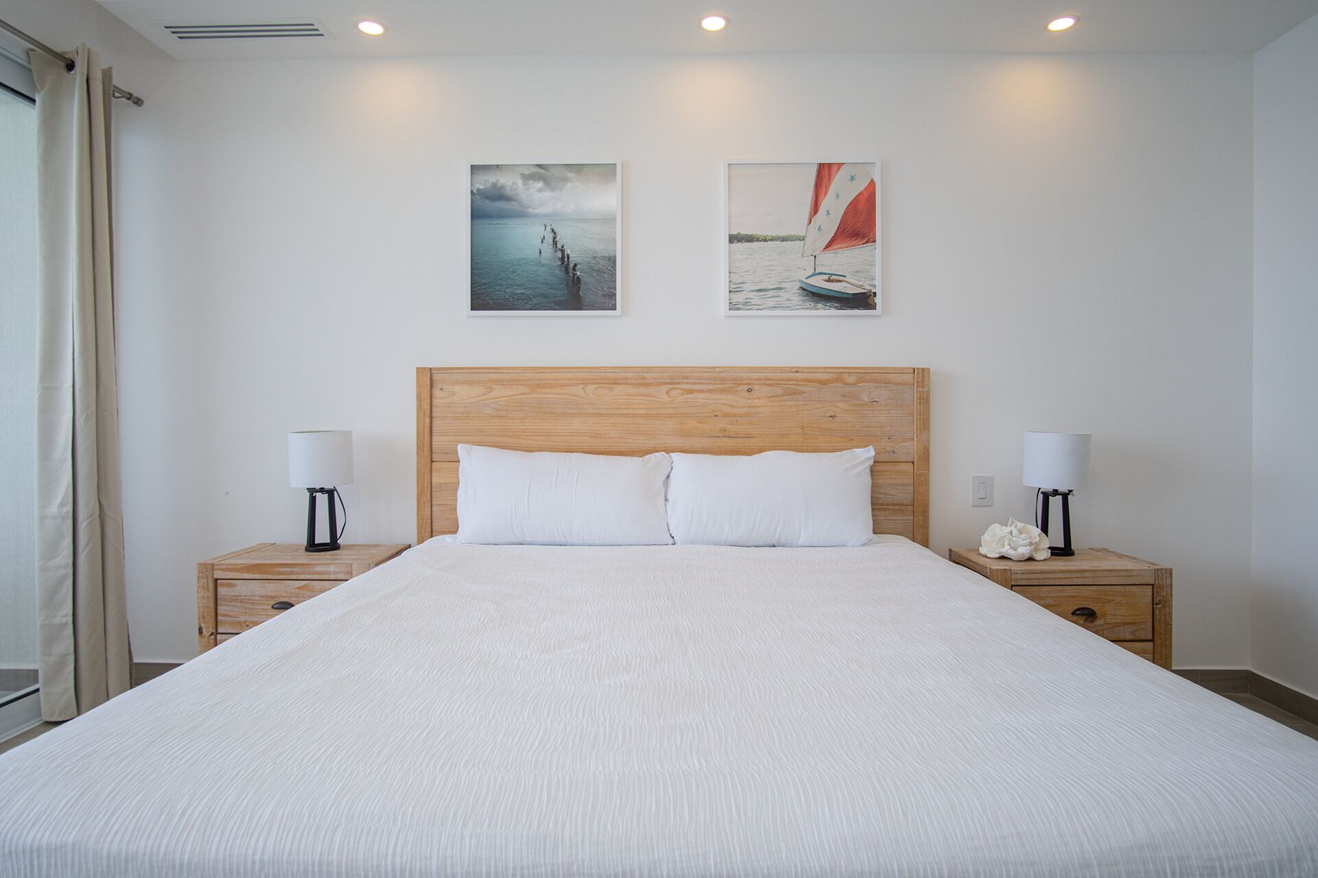 A large bed with a wooden headboard, two bedside tables with lamps, and two wall-mounted paintings of sailboats.
