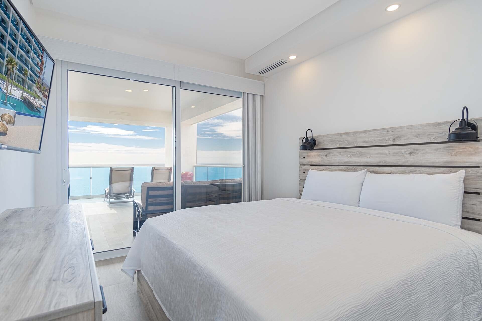 Un dormitorio con una cama grande, cabecera de madera, una mesita de noche y vistas al balcón.