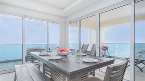 Un coin repas avec vue sur la mer, comprenant une table en bois, des chaises et un saladier rempli de fruits.