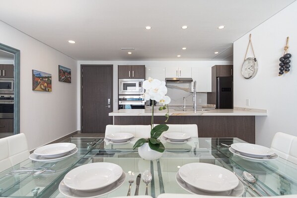A modern kitchen with dark cabinets, stainless steel appliances, and a glass dining table set for six.