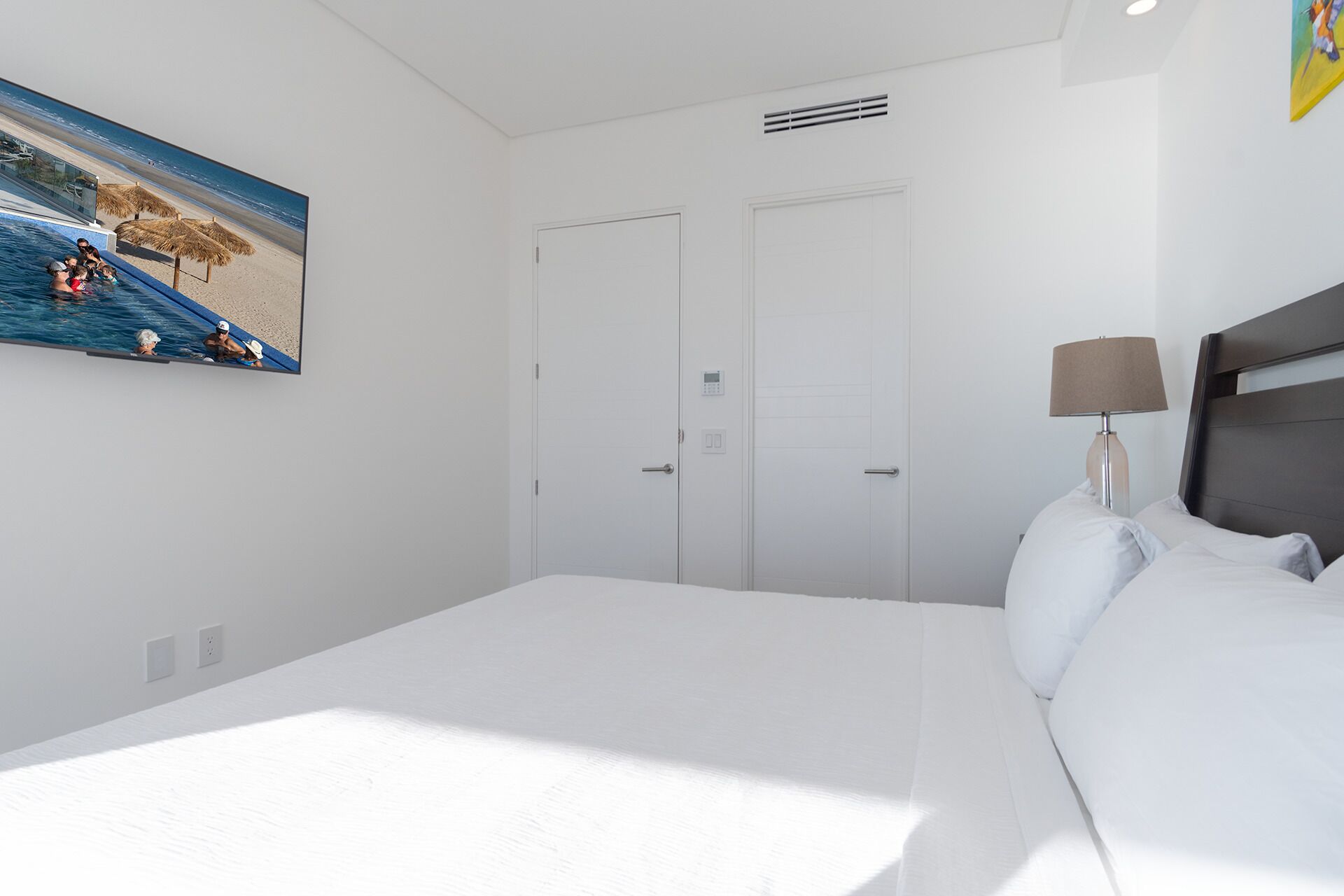 Une chambre d’hôtel avec un lit, une lampe de chevet, un tableau représentant une scène de plage et une porte dotée d’un système de verrouillage à clavier.