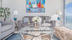 Un salon moderne avec un canapé gris, une table basse en verre et un tableau représentant des voiliers.