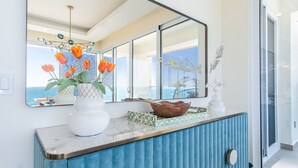 Una cocina moderna con encimera de mármol, un armario azul y un amplio ventanal con vista al mar.