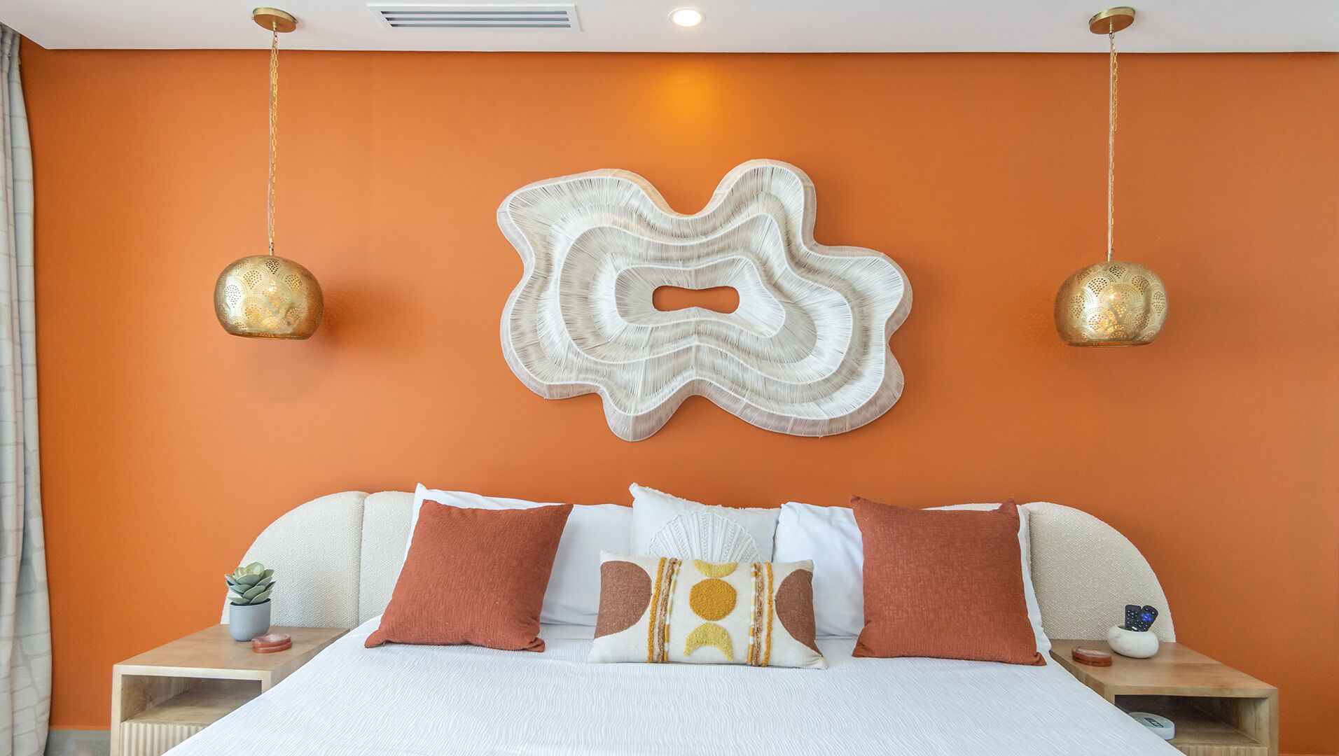 Une chambre d’hôtel avec un grand lit, deux tables de chevet, une œuvre d’art abstraite accrochée au mur et deux lampes suspendues.