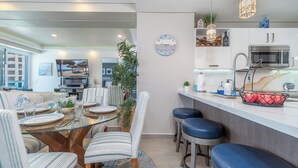 A modern kitchen with a microwave, sink, and countertop. There is a dining area with a glass table and striped chairs. - Sublime 1 Bedroom Condo Encantame Towers Verano 403 (Puerto Peñasco)