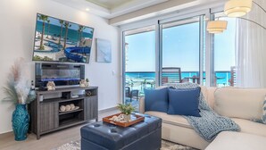 A modern living room with a large TV, a sofa, and a view of the beach. - Sublime 1 Bedroom Condo Encantame Towers Verano 403 (Puerto Peñasco)