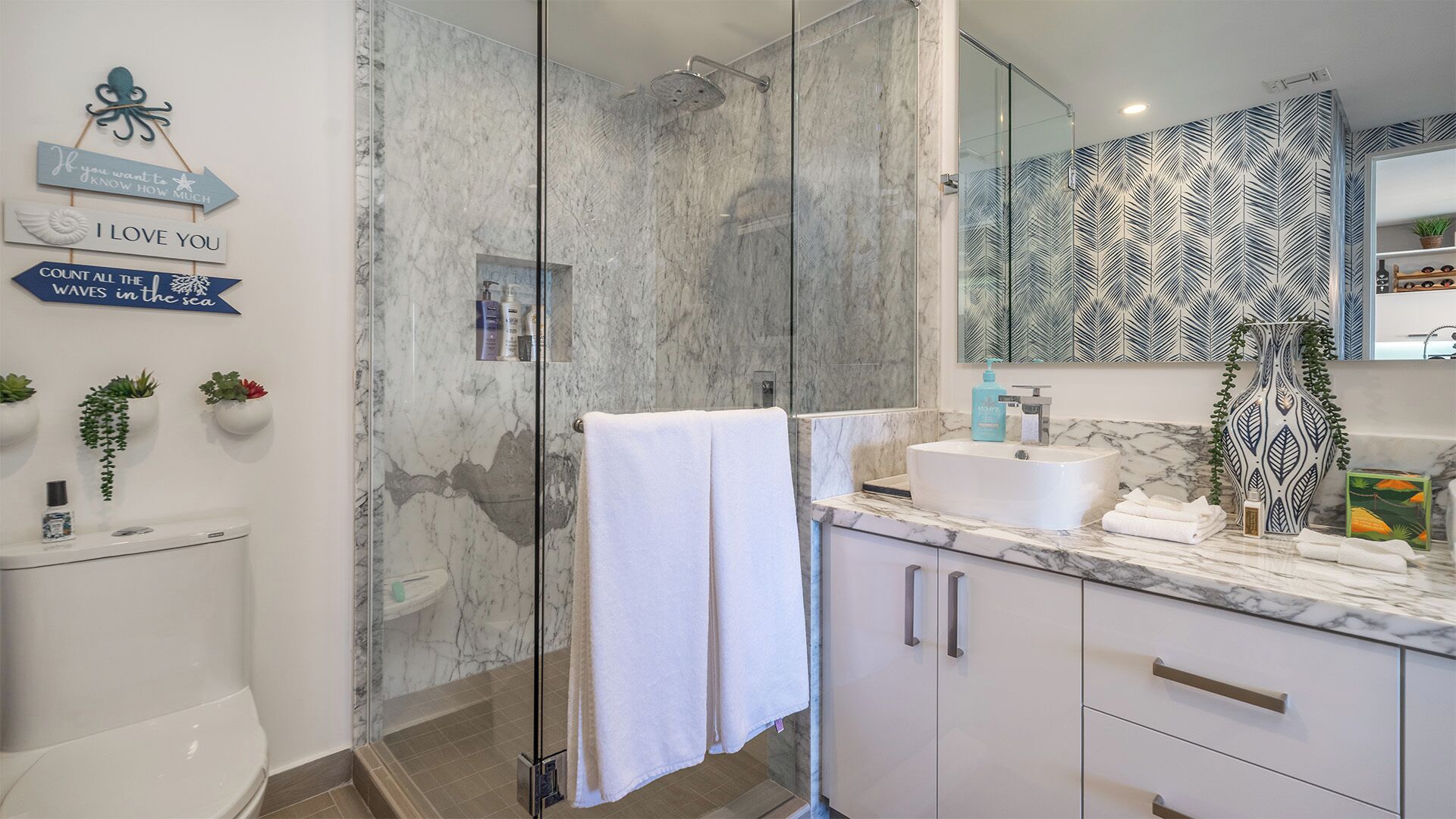 A modern bathroom with a glass shower enclosure, marble walls, and a vanity with a sink and mirror.